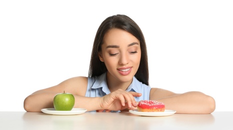 Woman choosing between apple and doughnut at table on white background