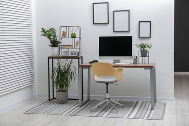 Photo of Cozy workspace with computer on desk, chair and houseplants near white wall at home