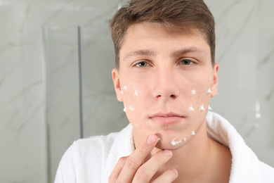 Photo of Teen guy with acne problem applying cream in bathroom