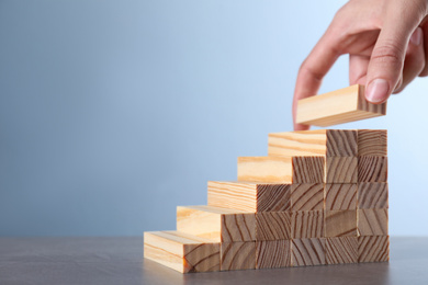 Photo of Woman building steps with wooden blocks at grey table, closeup. Career ladder