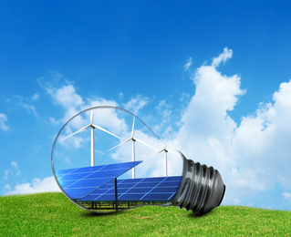Alternative energy source. Light bulb with solar panels and wind turbines outdoors