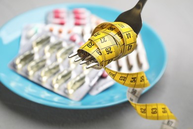 Fork with measuring tape and blurred pills on background, closeup. Weight loss