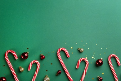 Candy canes and Christmas balls on green background, flat lay. Space for text