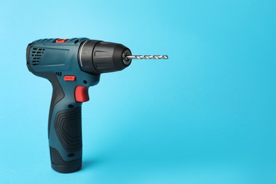 Modern electric power drill on light blue background, space for text
