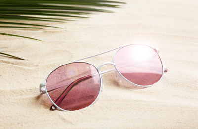 Stylish sunglasses and tropical leaf on white sand. Vacation time