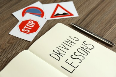 Workbook for driving lessons, pen and road signs on wooden table, closeup. Passing license exam