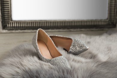 Stylish shiny high heeled shoes on faux fur near mirror in room