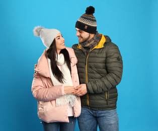 Happy young couple in warm clothes on blue background. Winter vacation
