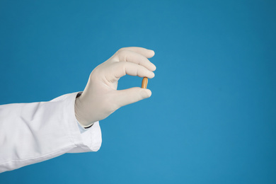 Doctor holding suppository for hemorrhoid treatment on blue background, closeup