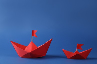 Handmade red paper boats with flags on blue background. Origami art