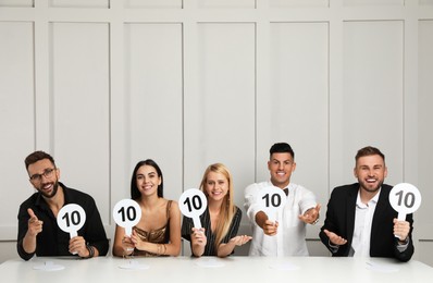 Panel of judges holding signs with highest score at table against light wall