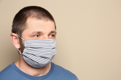Man wearing handmade cloth mask on beige background, space for text. Personal protective equipment during COVID-19 pandemic