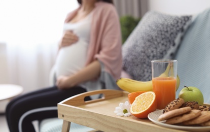 Tray with fresh fruits, cookies and pregnant woman on background