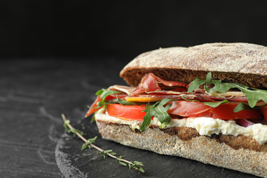 Photo of Delicious sandwich with fresh vegetables and prosciutto on black table, closeup. Space for text