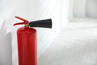 Fire extinguisher near white wall indoors. Space for text