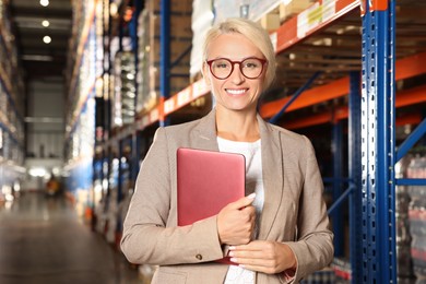 Happy manager holding modern tablet in warehouse with lots of products