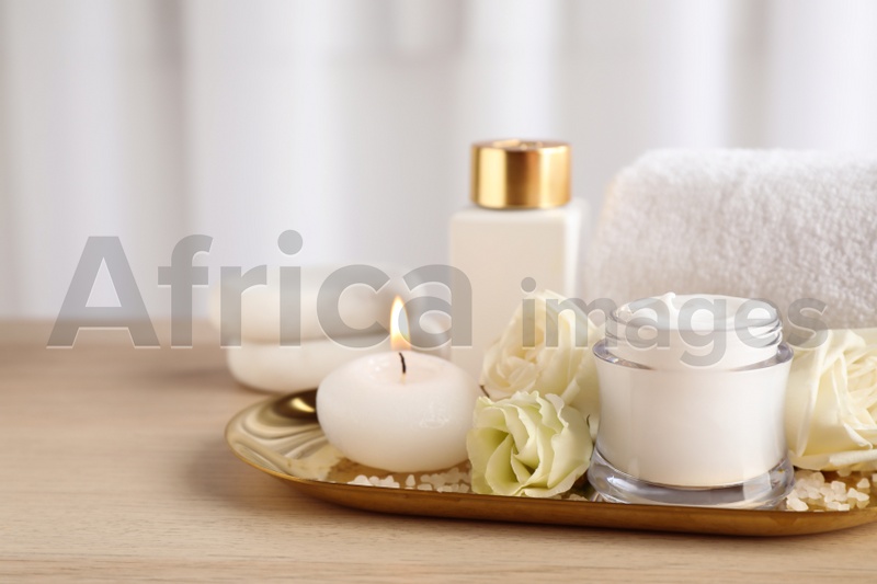 Spa composition with skin care products, flowers and candle on wooden table. Space for text