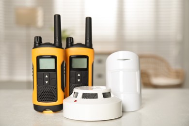 Photo of Walkie talkies, smoke and movement detectors on white table indoors. Home security system