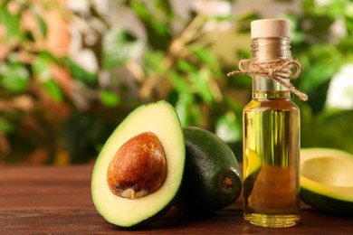 Photo of Glass bottle of cooking oil and fresh avocados on wooden table against blurred green background, space for text