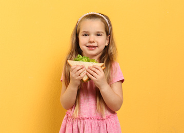 Photo of Cute little girl with tasty sandwich on yellow background