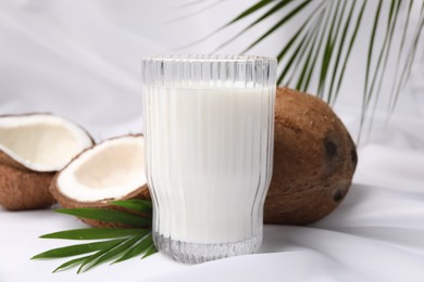 Photo of Glass of delicious coconut milk, palm leaves and coconuts on white fabric