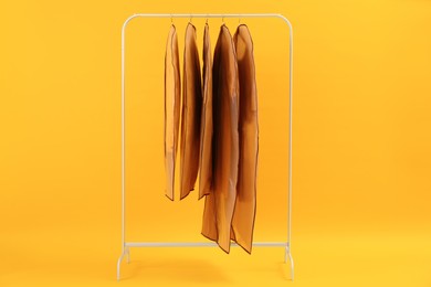 Garment bags with clothes on rack against yellow background