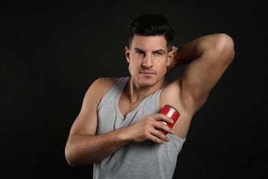 Photo of Handsome man applying deodorant to armpit on black background