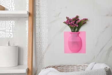 Silicone vase with flowers on white marble wall in bathroom