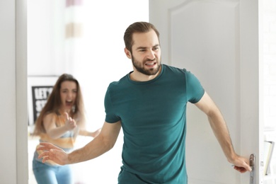 Young man walking out of door during argument with his girlfriend indoors