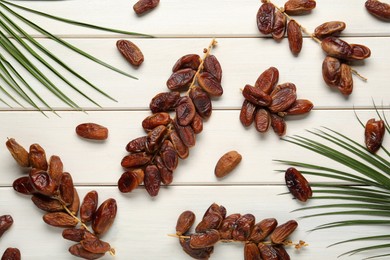 Sweet dried dates with palm leaves on white wooden table, flat lay