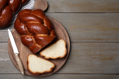Photo of Cut homemade braided bread and knife on wooden table, flat lay with space for text. Traditional Shabbat challah