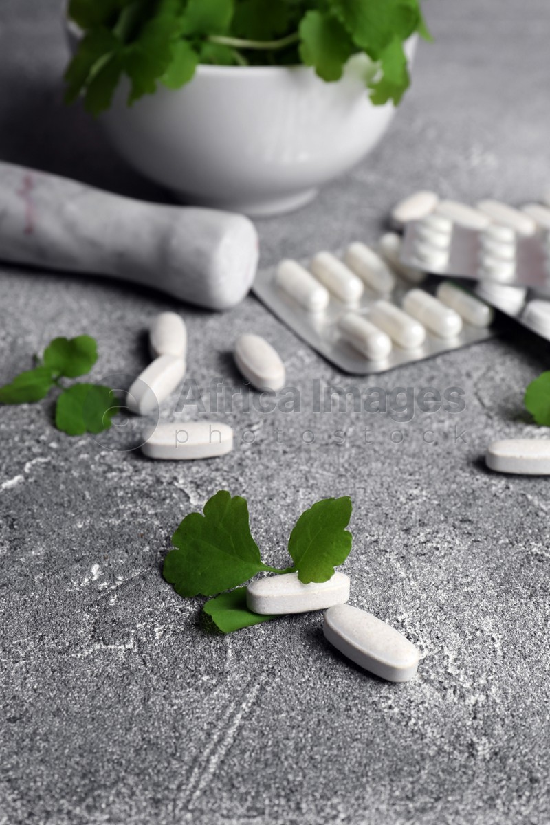 Pills and mortar with fresh green celandine on light grey table
