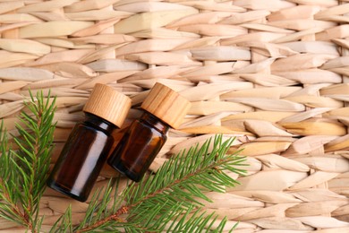 Bottles of pine essential oil and branches on wicker surface, flat lay. Space for text