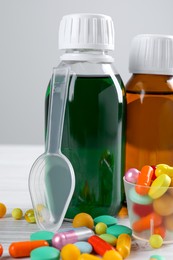 Photo of Bottles of syrups with pills on wooden table against white background, closeup. Cough and cold medicine