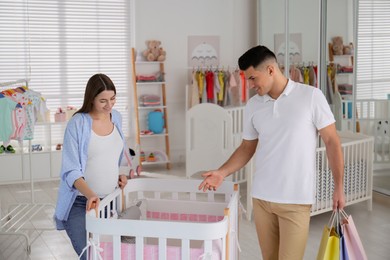 Happy pregnant woman and her husband with shopping bags choosing crib in store