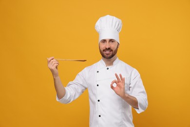 Photo of Smiling mature male chef with spoon showing ok gesture on orange background