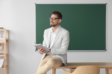 Happy teacher with book at desk in classroom