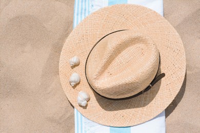Straw hat with seashells and beach towel on sand, top view. Space for text