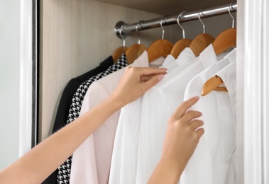 Woman taking shirt from wardrobe with stylish clothes, closeup view