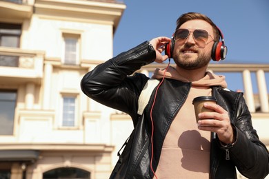 Happy young man with coffee and headphones listening to music on city street