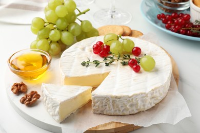 Brie cheese served with honey and berries on white table