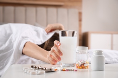 Woman taking medicine for hangover in bed at home, focus on hand with glass