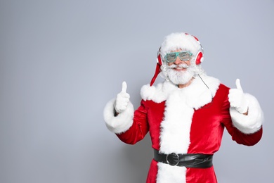 Santa Claus listening to Christmas music on color background