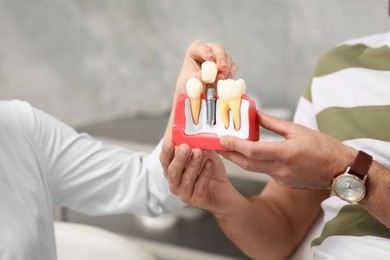 Doctor with educational model of dental implant consulting patient in clinic, closeup