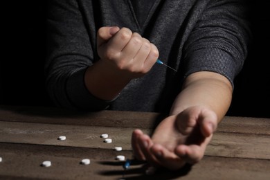 Photo of Addicted man with syringe near drugs at wooden table, closeup