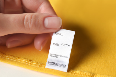 Woman reading clothing label with care symbols and material content on yellow shirt, closeup