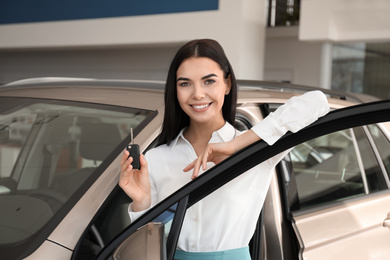 Photo of Saleswoman with key near car in dealership
