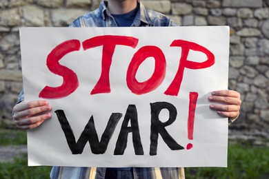 Photo of Woman holding poster with words Stop War against brick wall outdoors, closeup
