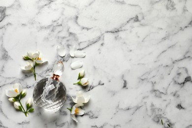 Bottle of luxury perfume and fresh jasmine flowers on white marble table, flat lay. Space for text